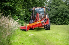 Zu sehen ist auf einer Rasenfläche ein Traktor mit Frontmährwerk beim Einsatz, welcher von einem Mitarbeiter des Bauhofes in Ahlerstedt bedient wird. Umrandet wird die Rasenfläche von Bäumen.