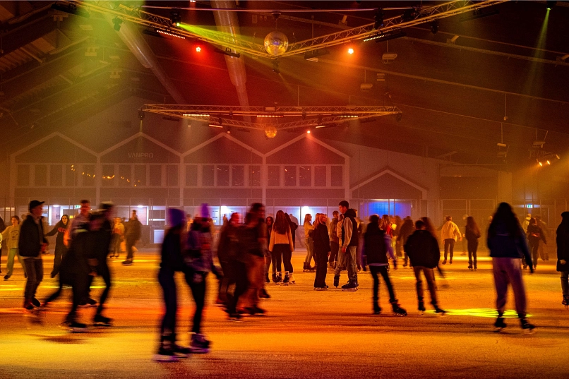 In orangenem Licht Schlittschuh fahrende Personen, Discobeleuchtung.