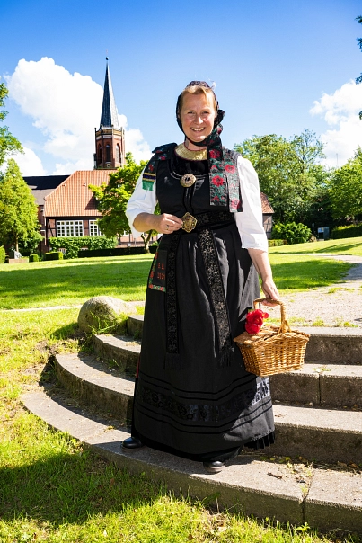 Eine Dame in historischer Geesttracht steht auf einer kleinen Treppe im Park, im Hintergrund ist ein Kirchturm zu sehen&nbsp;&copy;&nbsp;Martin Elsen