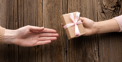Auf dem Bild sind zwei Hände zu sehen. Die Kinderhand übergibt ein kleines Geschenk, was mit einer Schleife verbunden ist.&nbsp;&copy;&nbsp;www.freepik.com