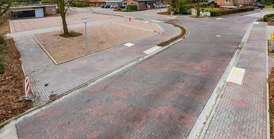 Rot gepflasterte Straße mit Linkskurve und sichtbarem Freibadvorplatz