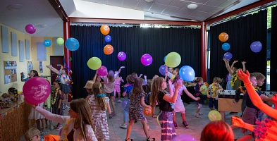Viele Kinder tanzen im Veranstaltungsraum. Sie werfen Luftballons in die Höhe.