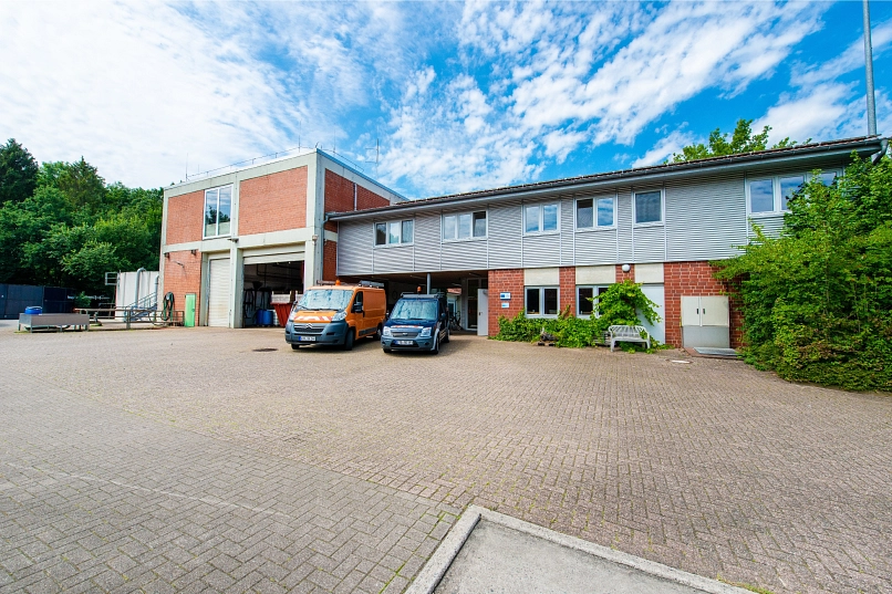 Zu sehen ist das Betriebsgebäude der Kläranlage Harsefeld samt angrenzendem Gebäudebereich, in welchem sich die Siebanlage und Eindicker I und II befinden. Davor parken die beiden Dienstfahrzeuge.