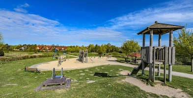 Spielplatz mit Turm und Rutsche im vordergrund, im Hintergrund ist ein Sandspielplatz mit weiteren Spielgeräten