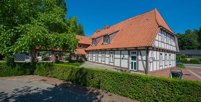 Hinter einer Hecke mit Baum ist das Künstlerhaus zum Felde in Harsefeld mit Eingang zum Stadtmarketing zu sehen.