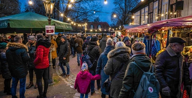 Personen auf vor verschiedenen Ständen am Abend des Winterzaubers 2022. An und über den Ständen sind leuchtende Lichterketten angebracht.