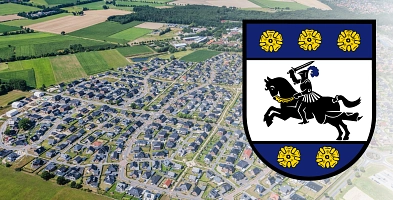 Luftbild von Harsefeld mit Neubaugebiet im Vordergrund. Rechts ist das Wappen des Flecken Harsefeld zu sehen.
