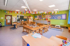 Ein Klassenzimmer einer Grundschule ist zu sehen mit Schultischen und Stühlen und eine fröhlich, bunte Wimpelkette hängt im Raum.