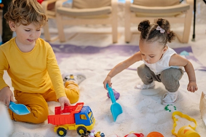 Auf dem Bild zu sehen sind zwei kleine Kinder, die ca. 1,5 Jahre alt sind und mit Baufahrzeugen im Sand spielen.&nbsp;&copy;&nbsp;Pexels Foto von Yan Krukau