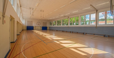 Turnhalle der Rosenborn Grundschule mit Parket, aufgezeichneten Feldlinien mit Matten und Tor im Hintergrund.