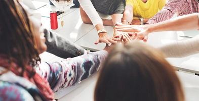 Menschen halten über einem Tisch ihre Hände übereinander als Team