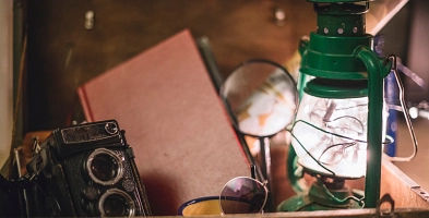 Eine Kiste, in der ein Buch, eine alte Kamera, eine Sonnenbrille, eine Lupe und eine Lampe liegen.