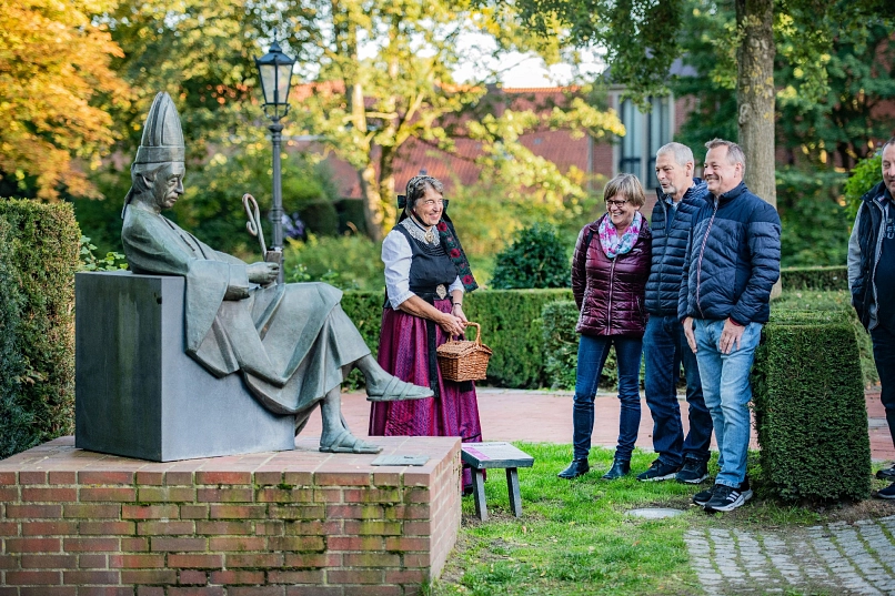 Eine Statue eines Abtes, daneben steht eine Dame in traditioneller Tracht von der Geest, um sie herum eine Reihe von zuhörenden Personen