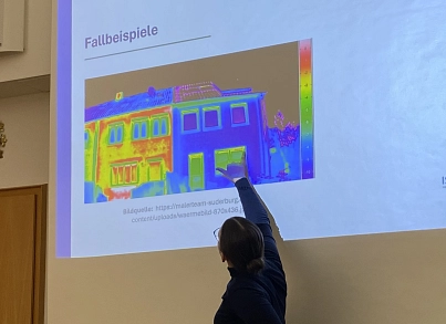 Auf einer Leinwand ist ein Haus mit den bunten Bildern einer Wärmebildkamera zu sehen. Davor steht eine Person, die sich zu dem Bild dreht und etwas darauf zeigt.&nbsp;&copy;&nbsp;Samtgemeindearchiv Harsefeld